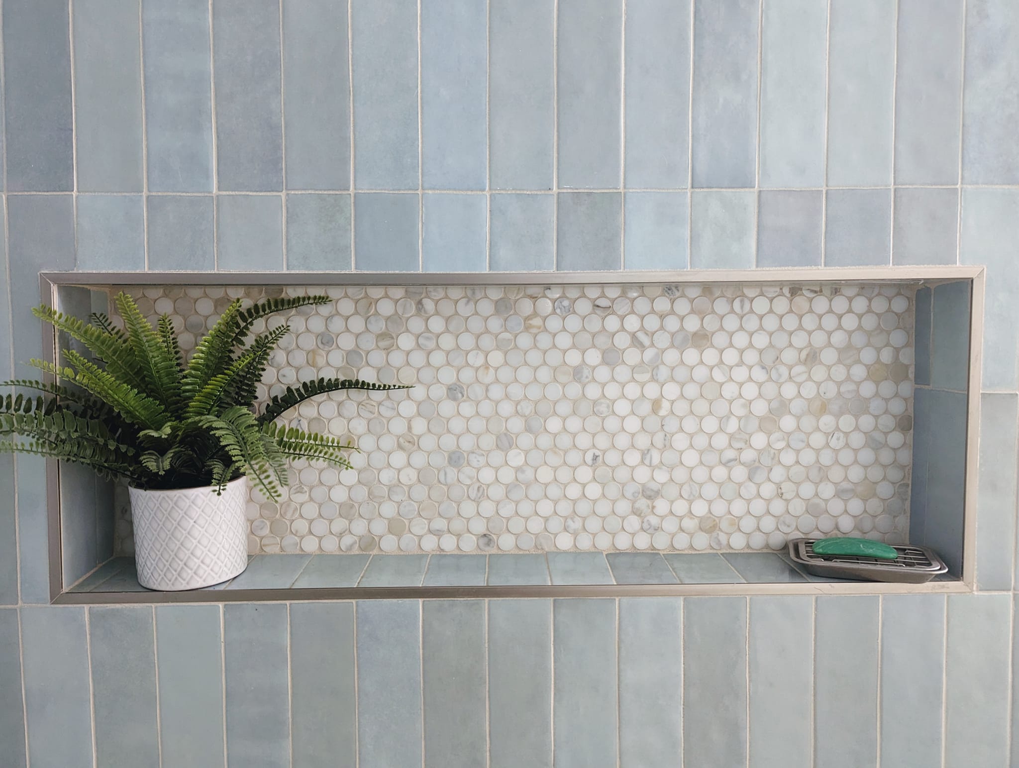 Beautiful, classic penny marble mosiacs in a shower niche with light blue vertically stacked blue tile.